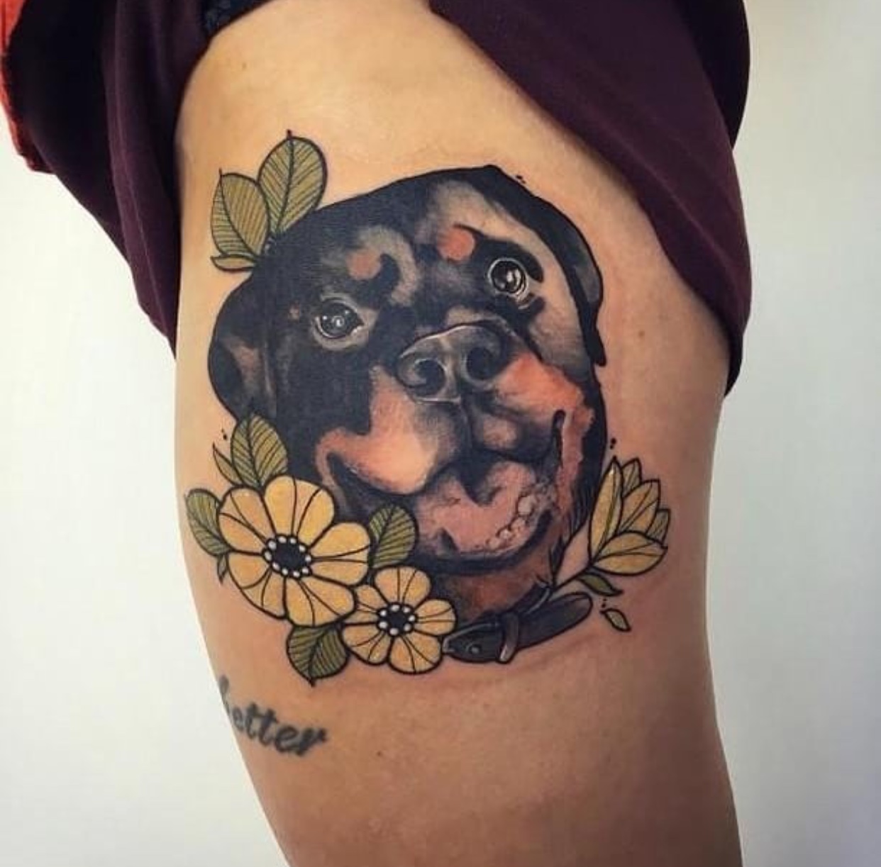 adorable face of a Rottweiler with flowers tattoo on thigh