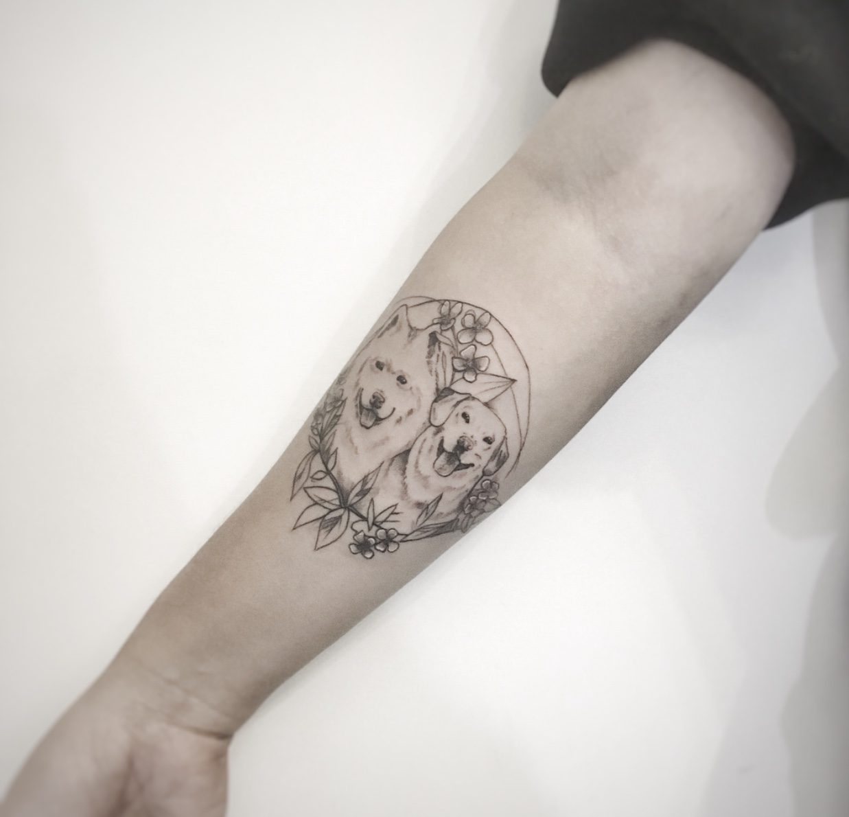 minimalist Labrador Retriever and another dog inside a floral circle tattoo on the forearm