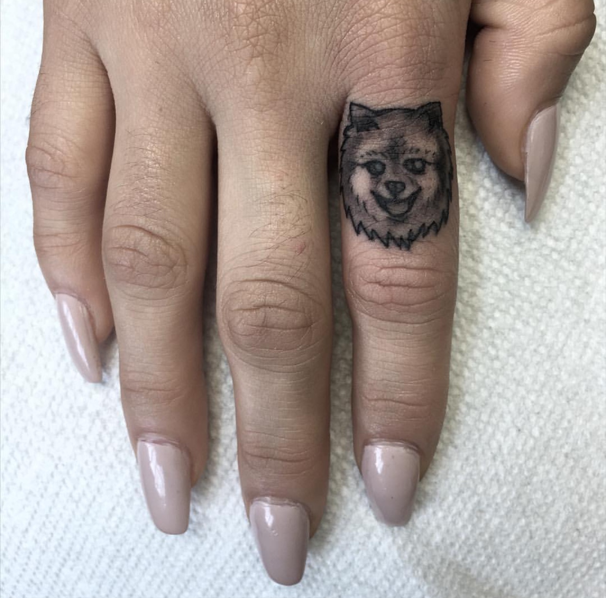 face of smiling Pomeranian small tattoo on the finger