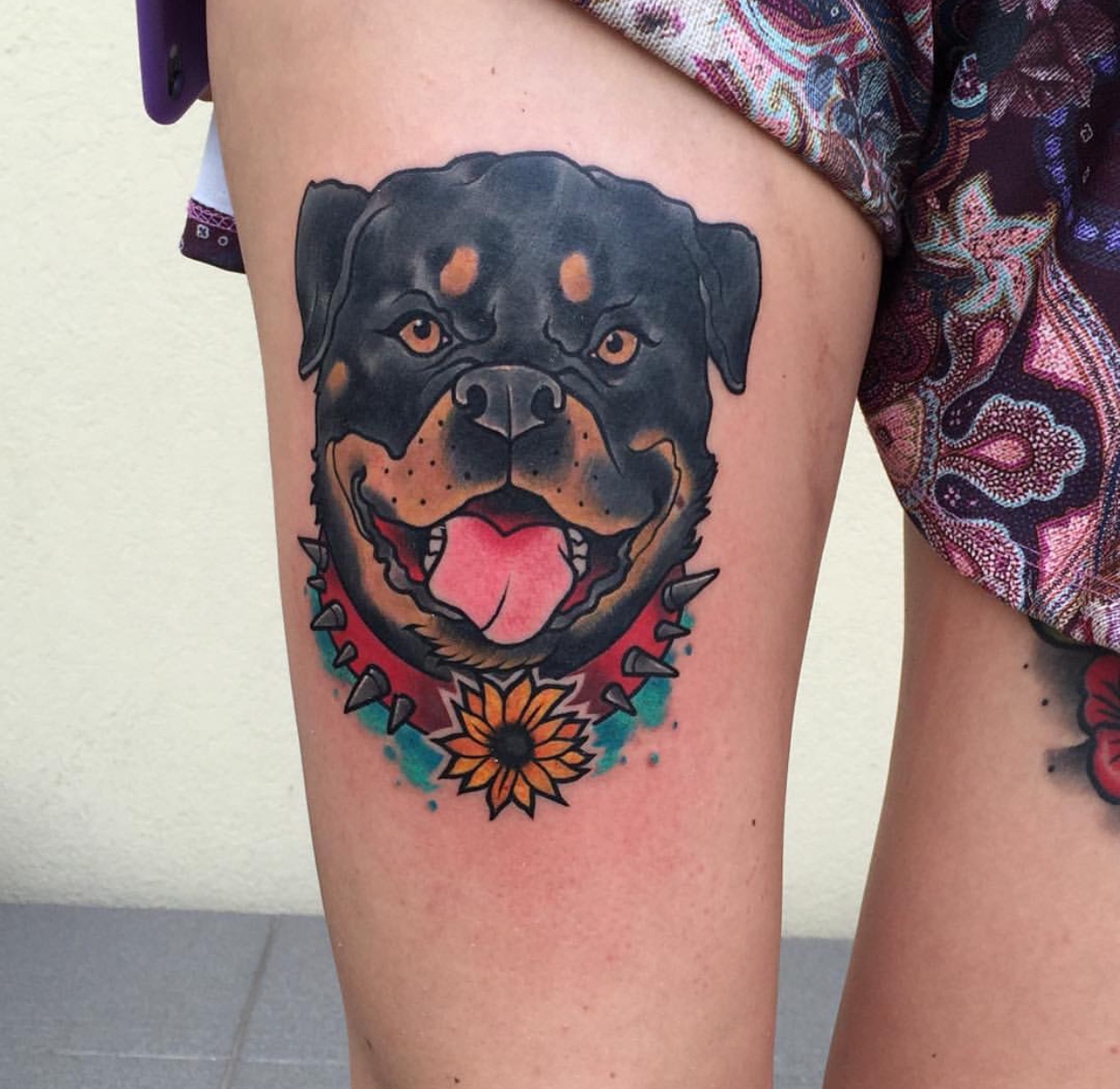 face of a Rottweiler wearing collar with horns and flowers tattoo on thigh