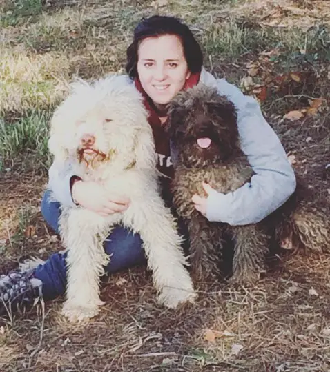 a woman sitting on the grass while embracing her two Lagotto Romagnolos