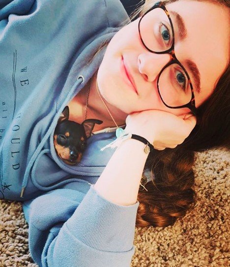 A woman lying on the carpet with a Miniature Pincher inside its sweater showing its face