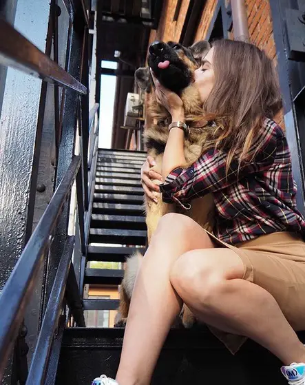 A woman sitting on the stairs while kissing her German Shepherd sitting beside her