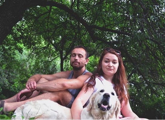 a man and a woman sitting under the tree with their Golden Retriever lying on the grass