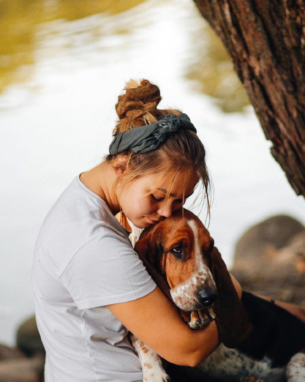A woman sitting by the lake while hugging her Basset Hound