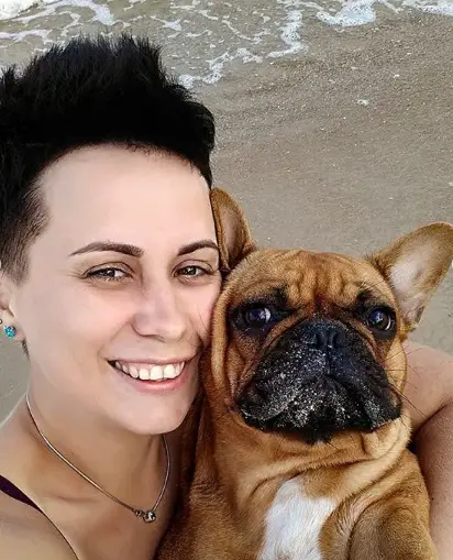 A woman at the beach taking a selfie with her French Bulldog