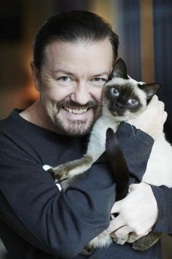 Ricky Gervais holding his Siamese Cat close to his face