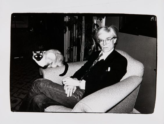 Andy Warhol sitting on the chair with his Siamese Cat on the arm of the chair