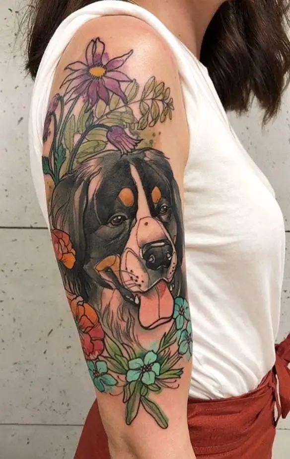 a cartoon face of a Bernese Mountain Dog and with flowers and leaves around it tattoo on the shoulder of a woman