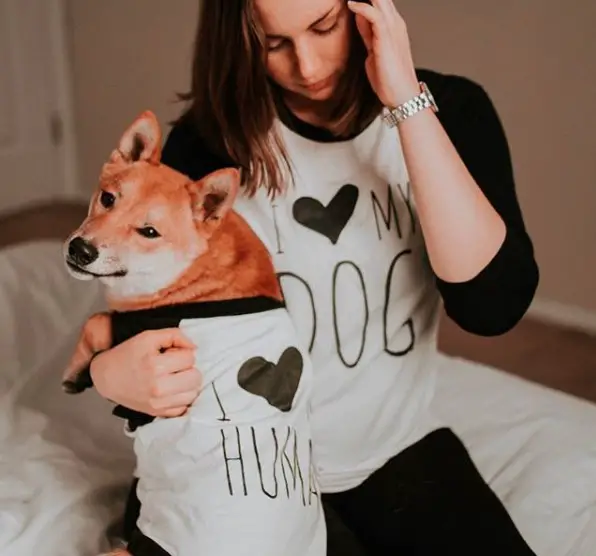A woman sitting on the bed wearing a long sleeved shirt matchy with her Shiba Inu