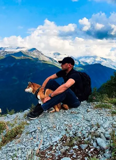 a man sitting on top of the mountain with his Shiba Inu