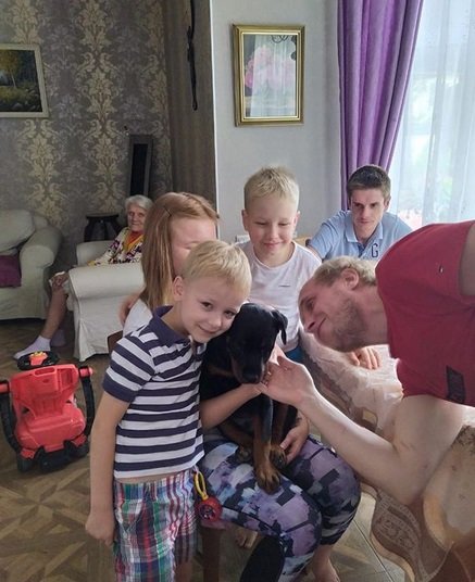 Rottweiler sitting on the lap of a young girl while being pet by other kids and a grown man