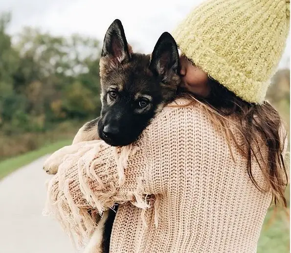 a woman standing in the road while holding and kissing a German Shepherd puppy