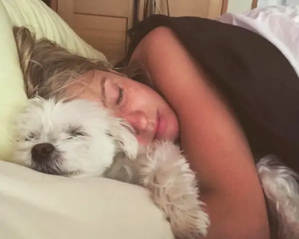 A woman sleeping on the bed while hugging her sleeping Maltese