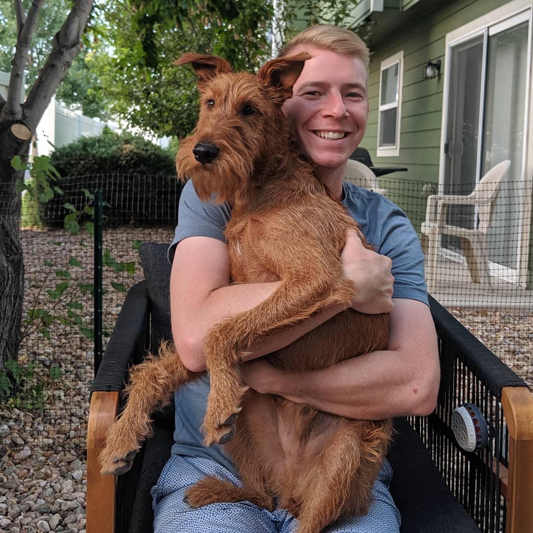 A man sitting on the chair while hugging his Irish Terrier sitting on his lap