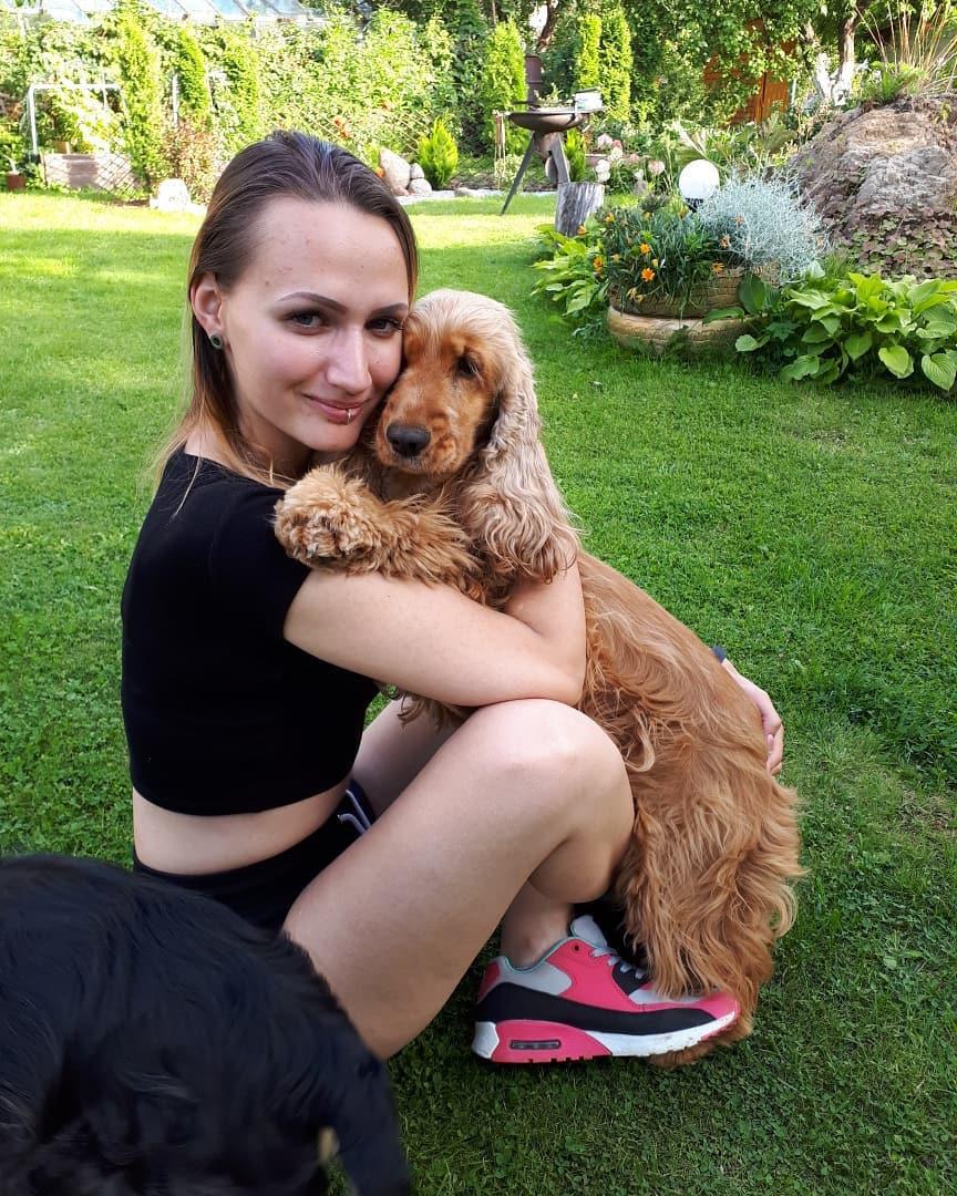 A woman sitting in the yard while hugging her Cocker Spaniel puppy