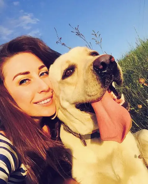 A woman in the field of grass taking a selfie with her Yellow Labrador