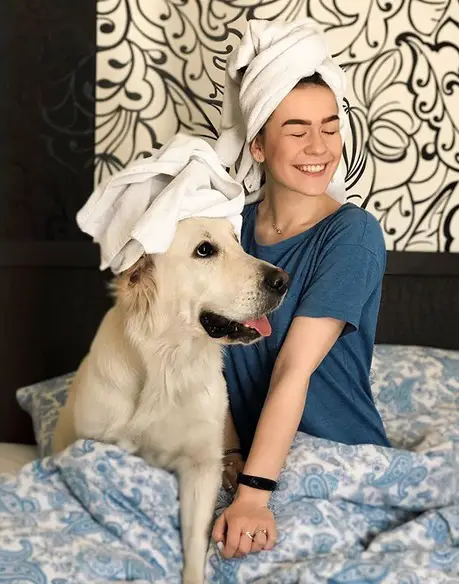 a woman with a towel wrapped around its head sitting on the next to a Golden Retriever who is also wearing a towel wrapped in its head